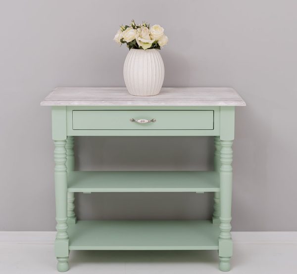 Landelijke smalle sidetable met 1 lade en 2 smalle planken voor opbergruimte. De sidetable heeft mooie lange klassieke poten en de lade gaat open door middel van een handgreep met bloemen erop. De onderkant van de kast heeft de kleur mint en het boven blad heeft de kleur white wash. De kast is gemaakt van massief eiken hout. De kast kan op verschillende manieren geverfd worden in verschillende kleuren en kan op maat gemaakt worden. Villa Laura